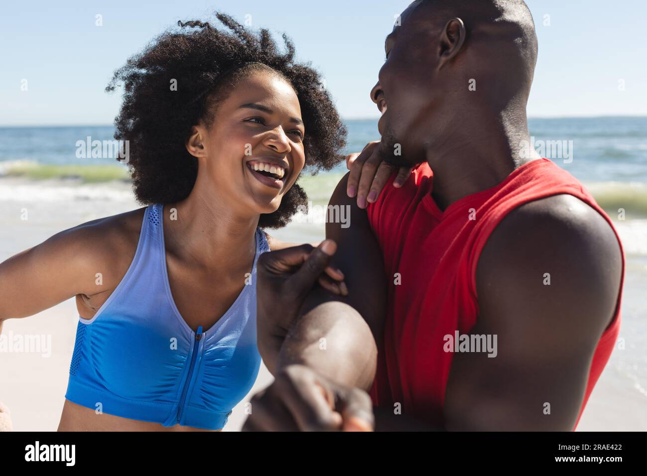 Coppia afro-americana in forma che si esercita, si allunga e sorride sulla spiaggia soleggiata Foto Stock