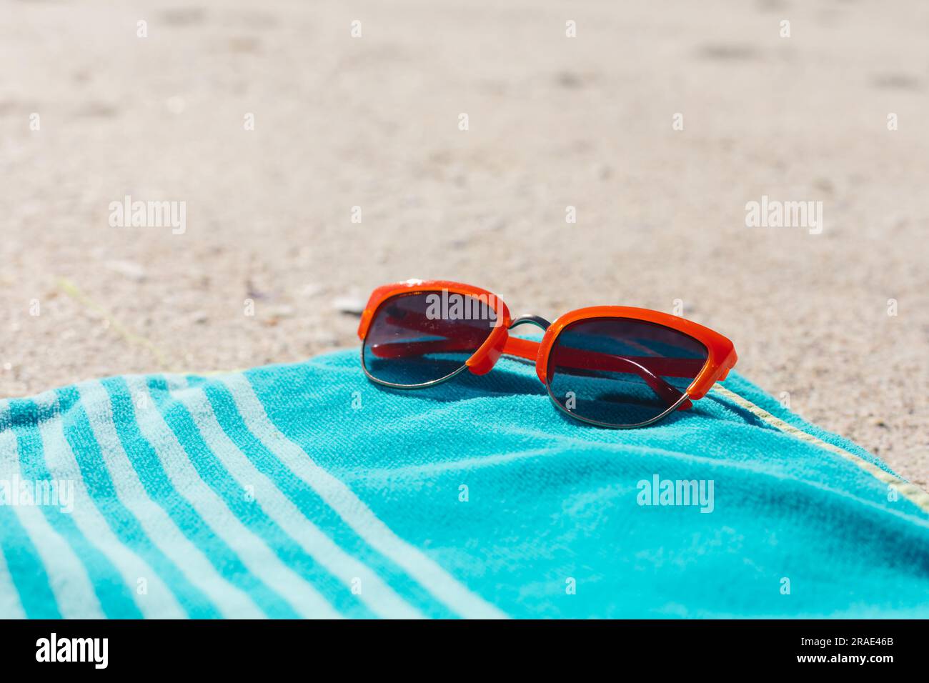Occhiali da sole rossi su un asciugamano a righe blu sulla spiaggia di sabbia soleggiata, spazio fotocopie Foto Stock