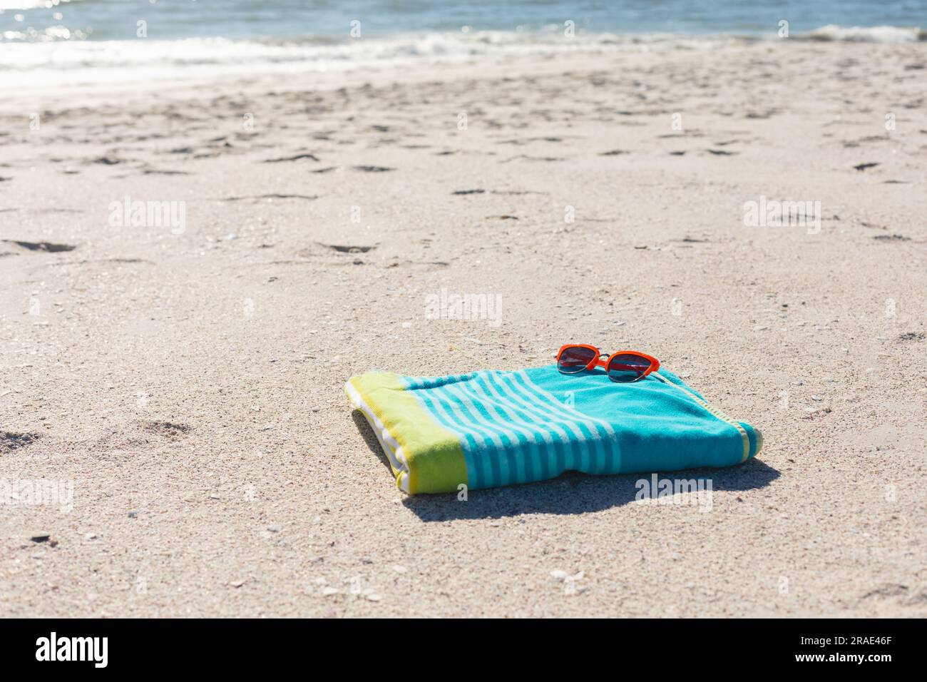 Occhiali da sole rossi su un asciugamano a strisce verdi e blu su una spiaggia di sabbia soleggiata vicino al mare, spazio fotocopie Foto Stock