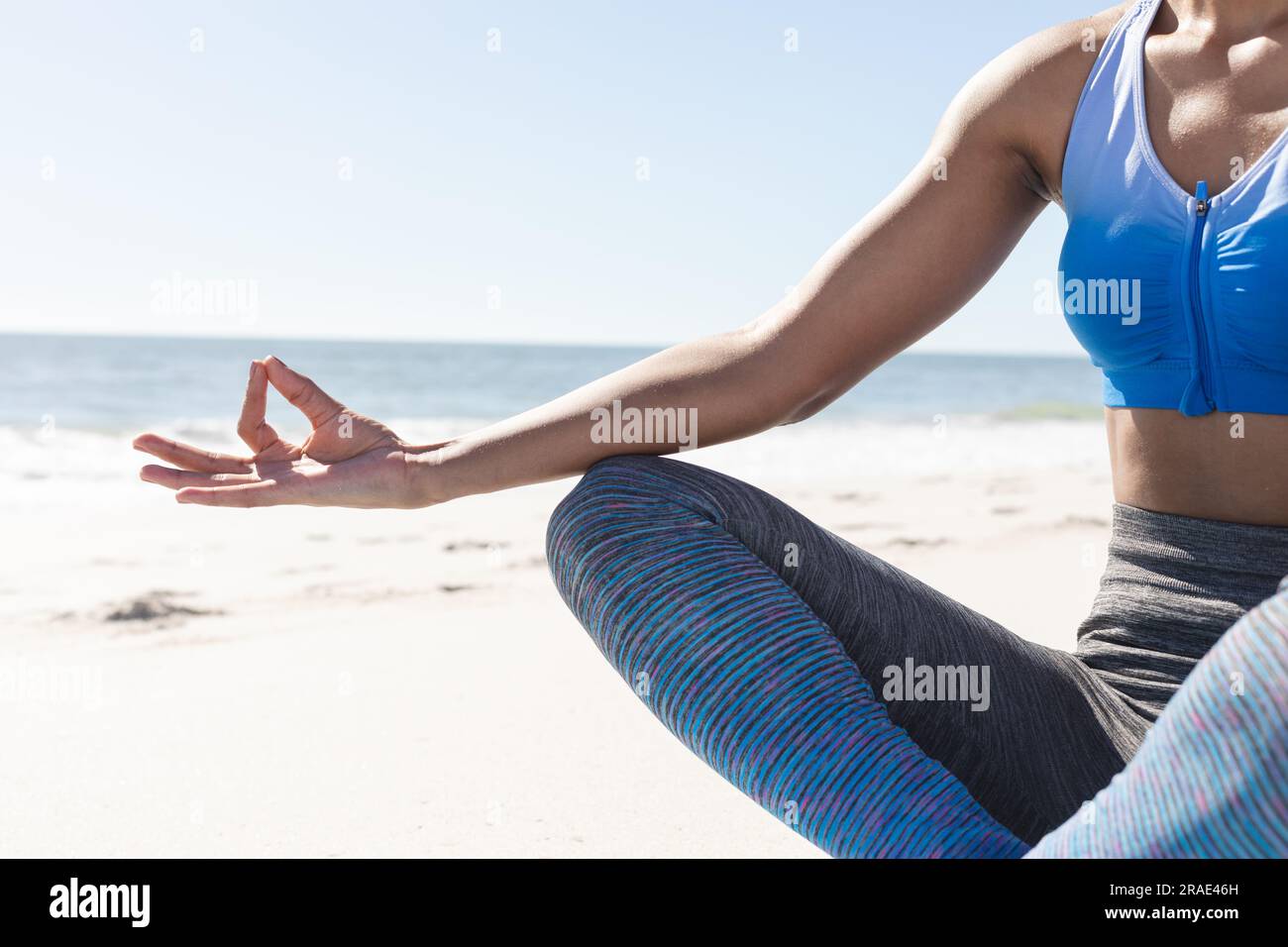 Sezione intermedia di una donna afroamericana in forma che pratica meditazione yoga seduto sulla spiaggia soleggiata Foto Stock