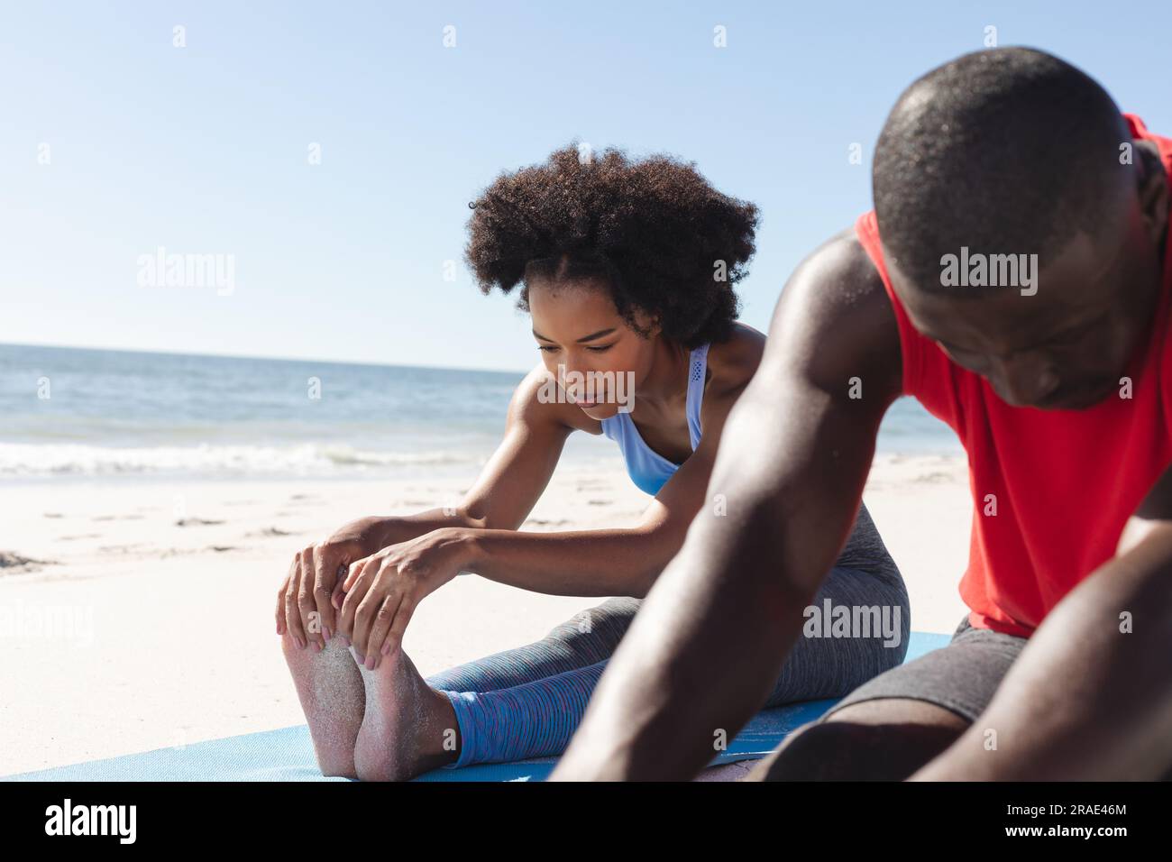 Allenati con una coppia afroamericana che pratica yoga, seduto e distendendosi sulla spiaggia soleggiata Foto Stock