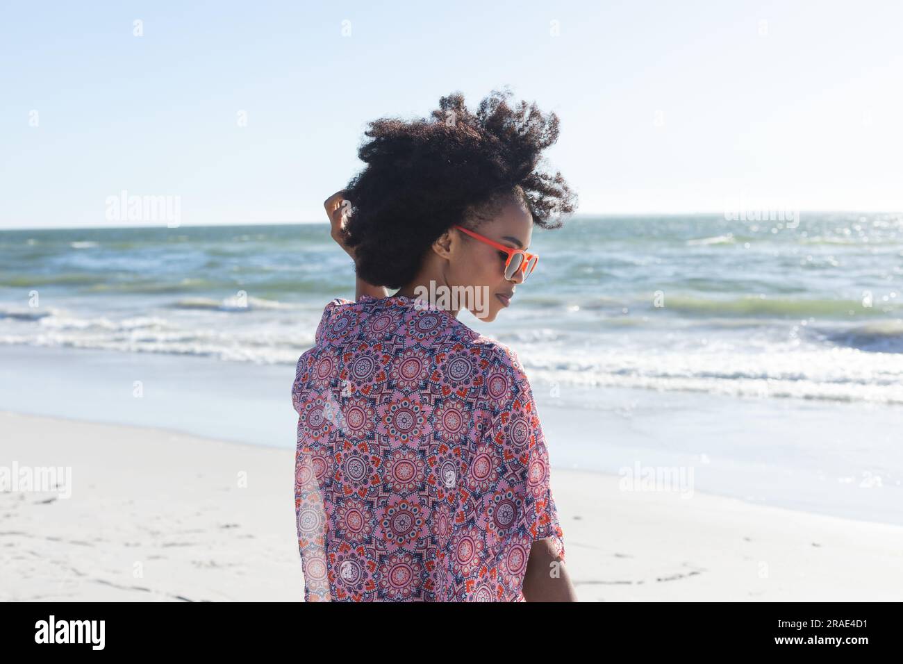 Felice donna afro-americana con occhiali da sole sorridente sulla spiaggia soleggiata in riva al mare Foto Stock