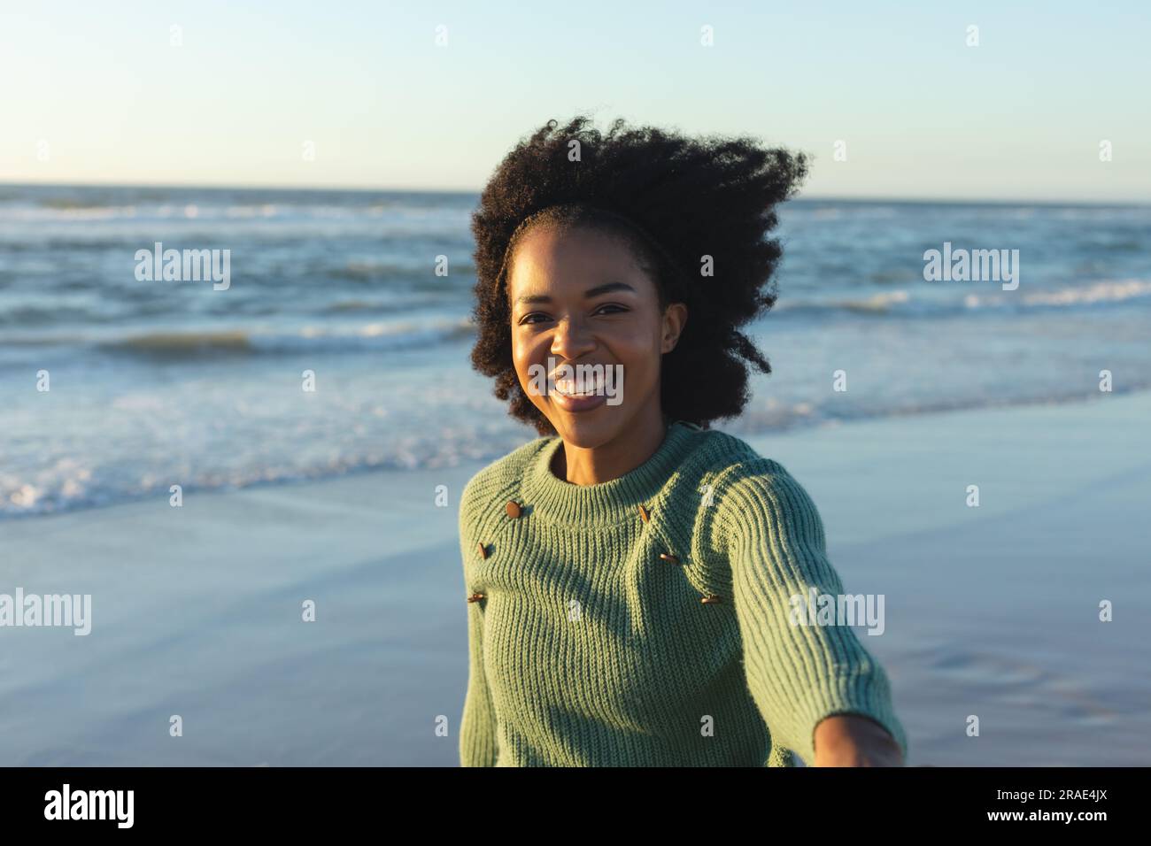 Ritratto di una donna afroamericana felice che guarda la macchina fotografica e sorride sulla spiaggia al tramonto Foto Stock