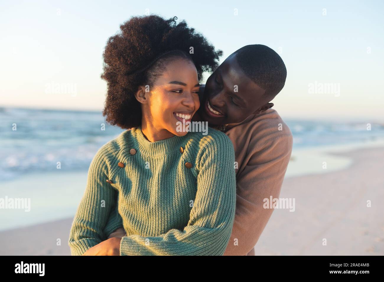 Felice coppia afro-americana che abbraccia e sorride sulla spiaggia soleggiata Foto Stock