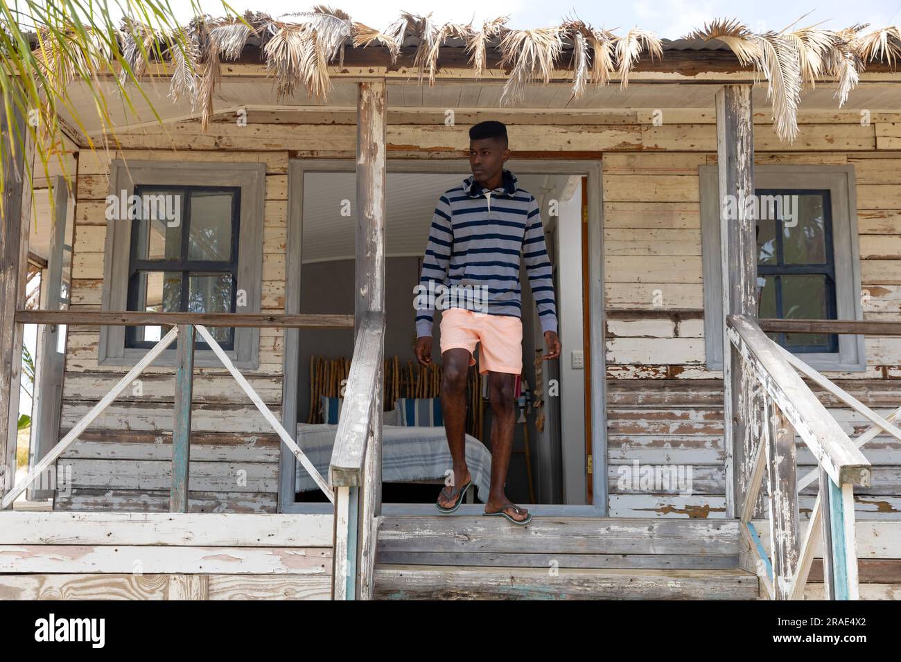 Uomo afro-americano che cammina lungo i gradini dal portico di una casa sulla spiaggia di legno, guardando lontano, spazio fotocopie Foto Stock