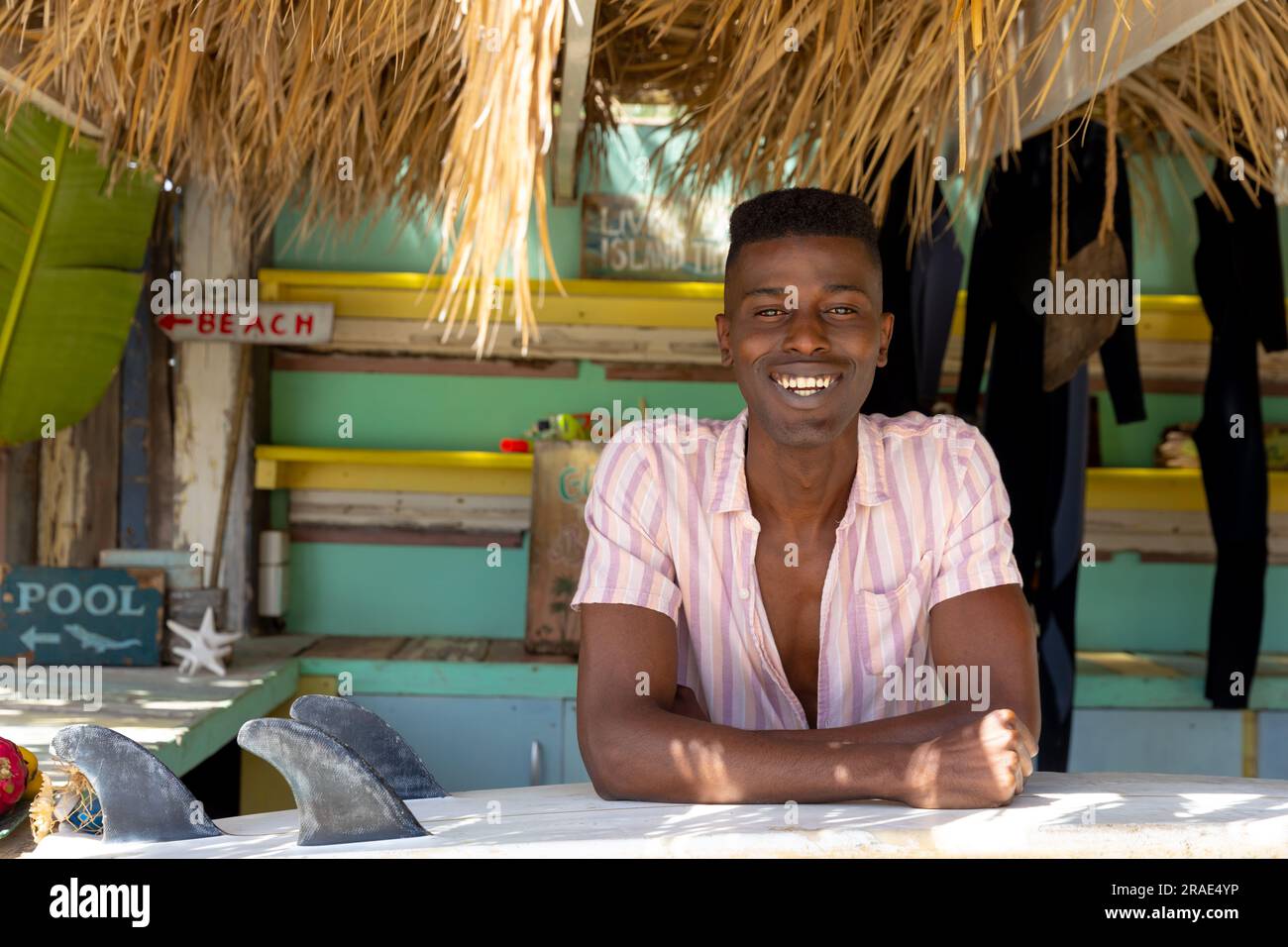 Ritratto di un uomo afro-americano seduto dietro il bancone della baracca da spiaggia di noleggio surf Foto Stock