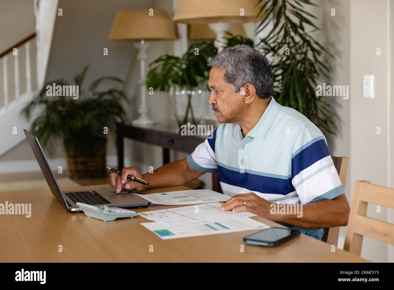 Uomo birazziale anziano che fa documenti e usa un computer portatile in sala da pranzo Foto Stock