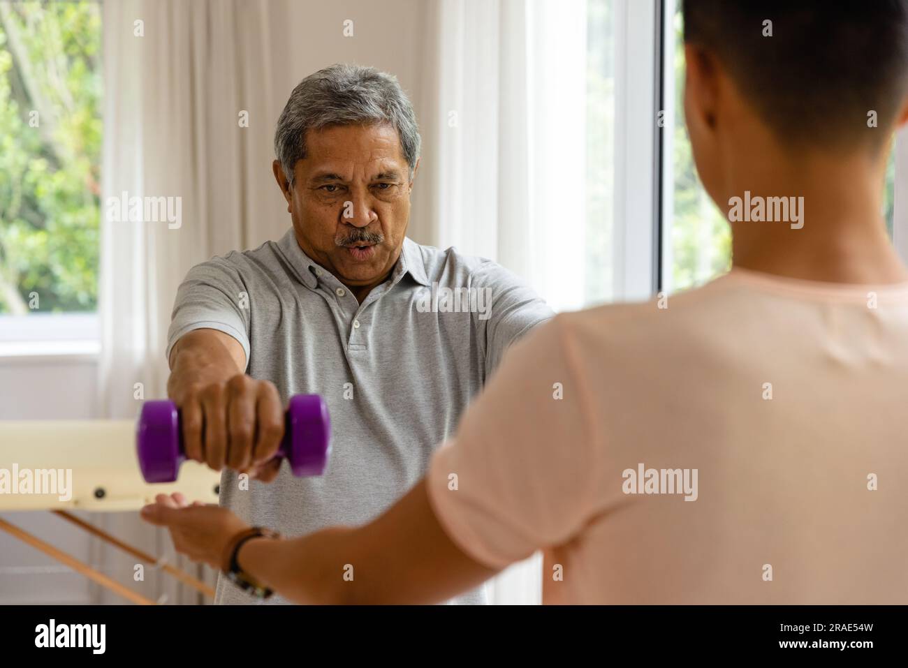 Fisioterapista maschile eterogeneo che consiglia e determina un paziente maschile anziano con manubri Foto Stock