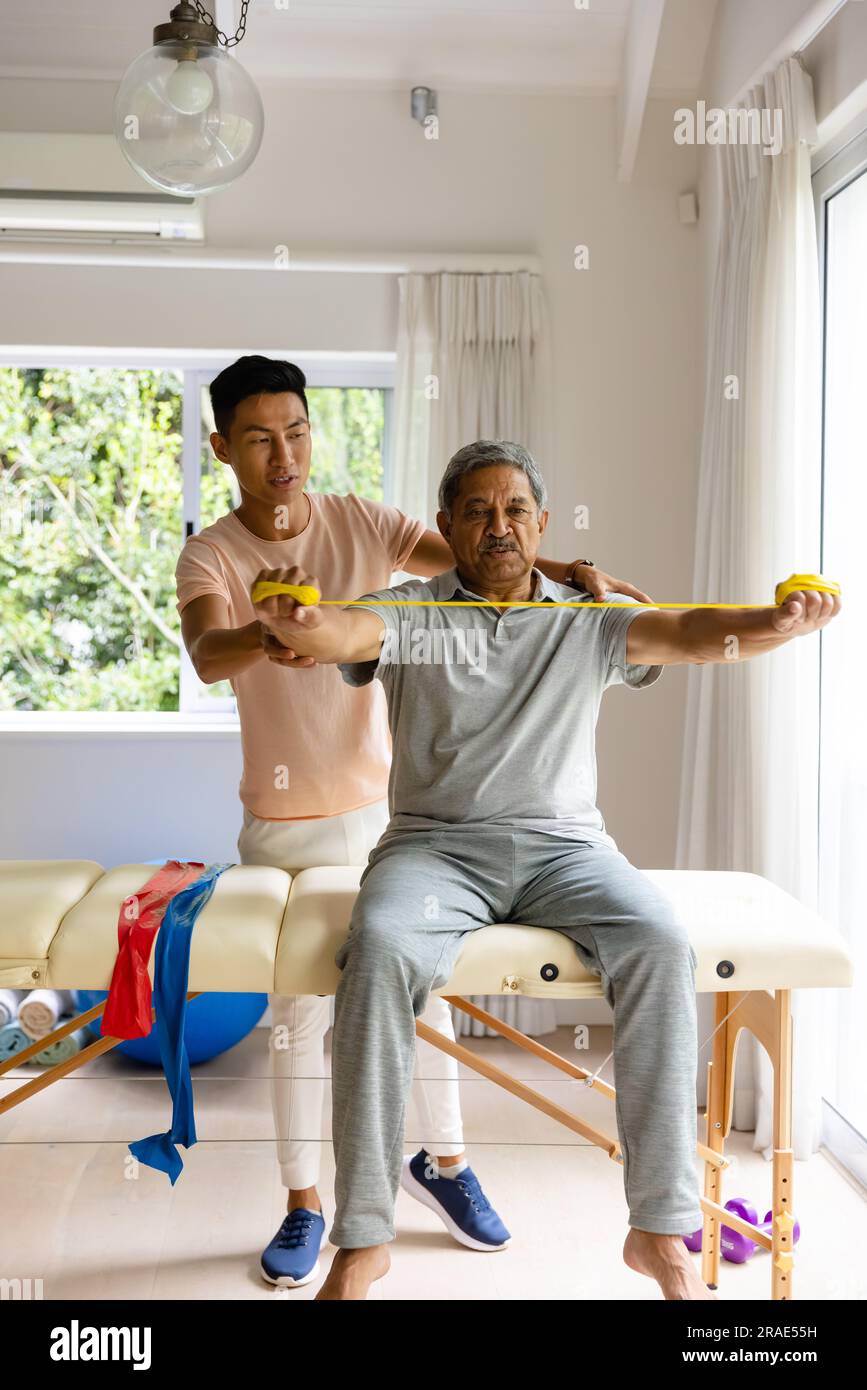 Fisioterapista maschile eterogeneo che consiglia e paziente anziano di sesso maschile che utilizza la fascia da ginnastica Foto Stock