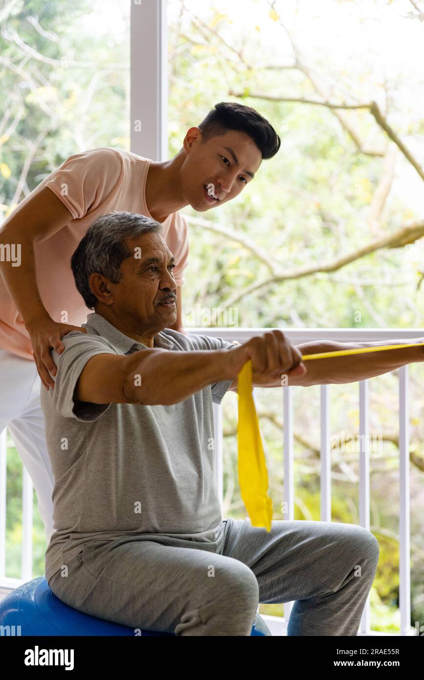Fisioterapista maschile felice eterogeneo che consiglia e paziente di sesso maschile anziano che utilizza la fascia da ginnastica Foto Stock
