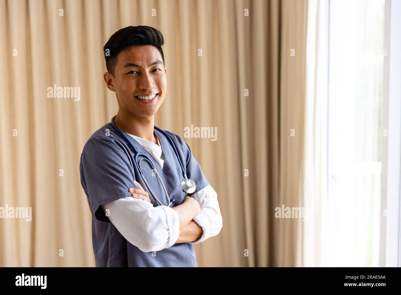 Ritratto di un medico maschio asiatico felice contro la tenda beige con spazio per la copia Foto Stock