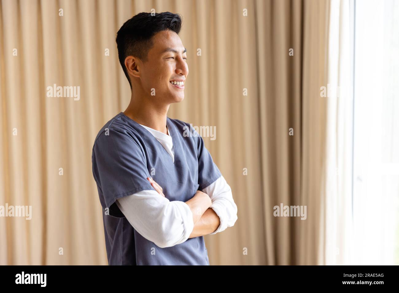 Profilo del medico maschio asiatico felice contro la tenda beige con spazio per la copia Foto Stock