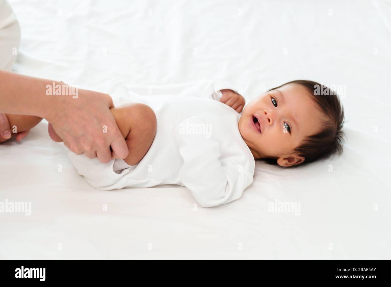 le mani di una madre che tiene le gambe del bambino e fa qualche esercizio giocoso su un letto Foto Stock