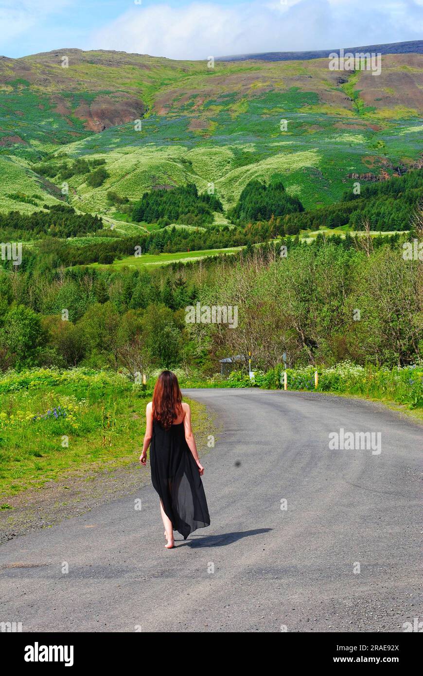 Una donna con un vestito nero scorrevole cammina lungo un sentiero verso il Monte Esja, Islanda, in una fresca giornata estiva. Foto Stock