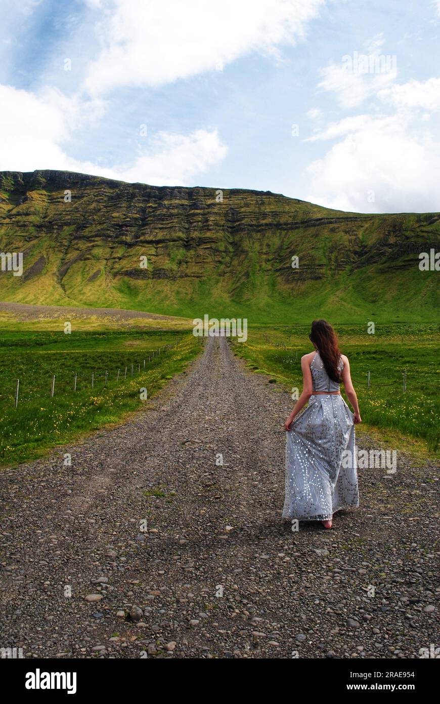 Una donna con un vestito scorrevole cammina su un sentiero verso una montagna vicino a Mossfellsbaer, Islanda, in una fresca giornata estiva. Foto Stock
