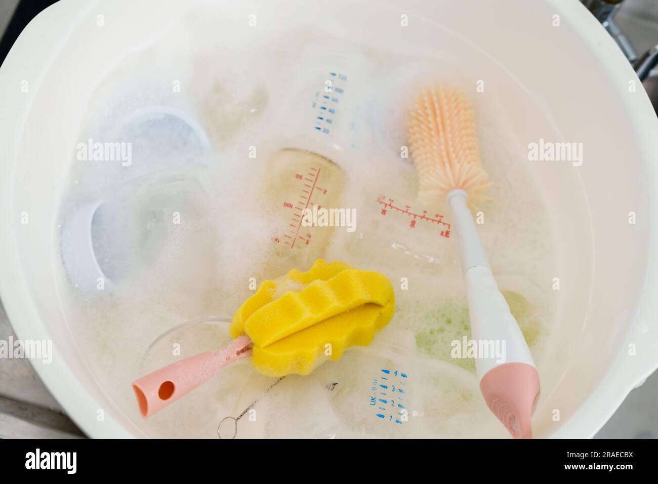 il biberon di latte con spazzola viene lavato in una vaschetta di plastica Foto Stock
