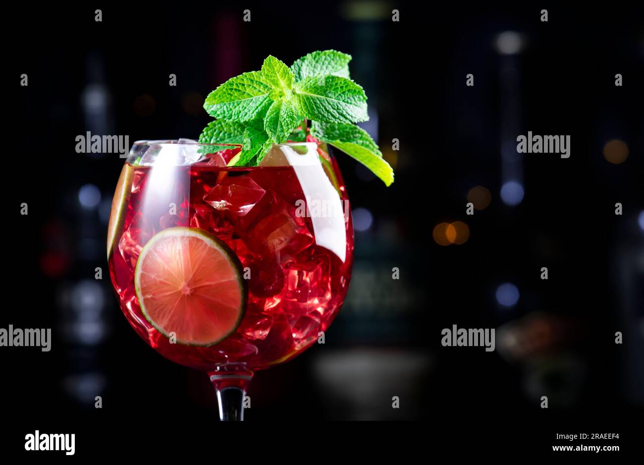 Cocktail alcolico Royal limonade con tequila, gin secco, rum bianco, vodka, liquore, lime, lamponi e ghiaccio nel bicchiere da vino. Bancone bar nero ba Foto Stock
