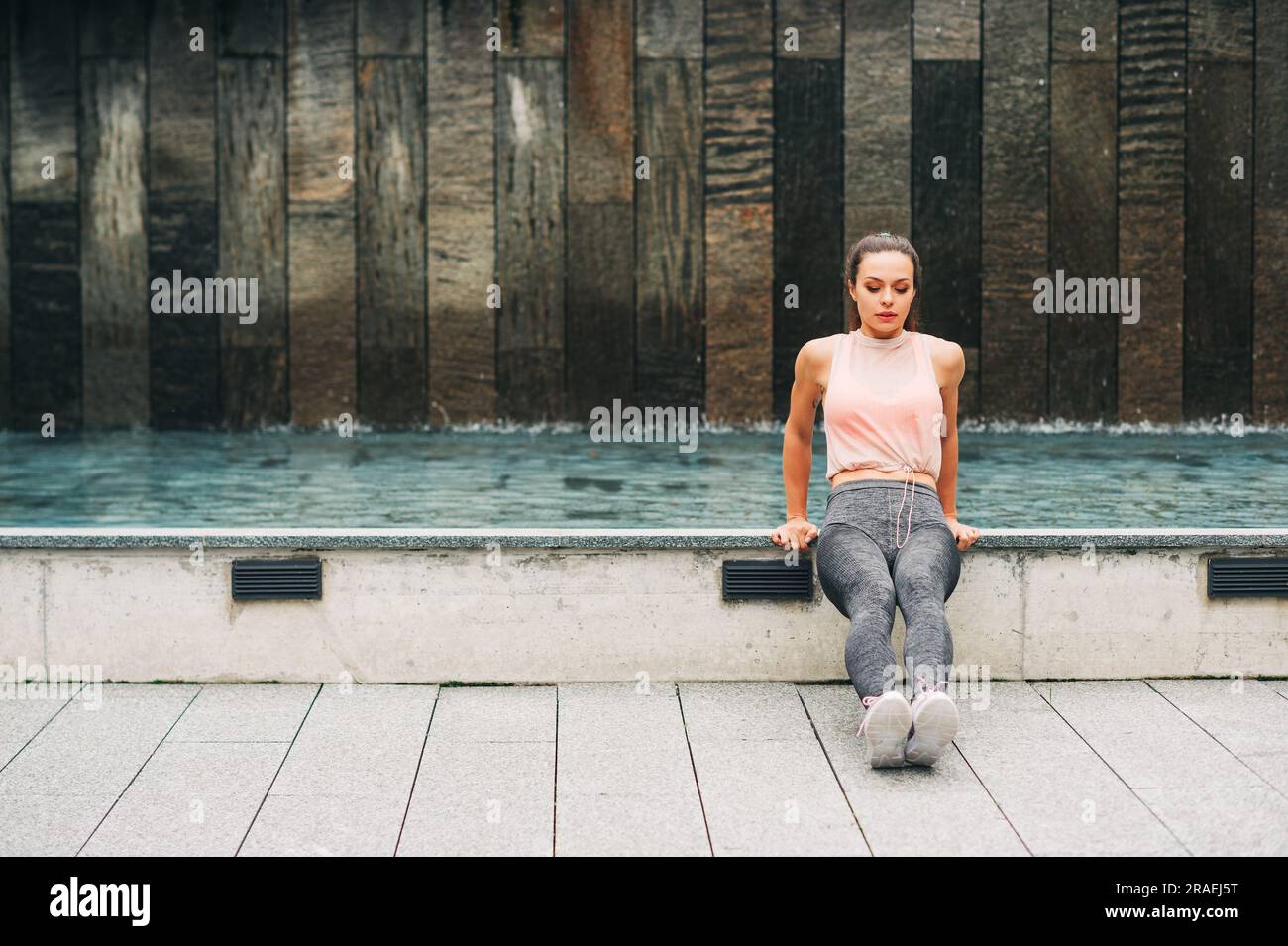 Ritratto all'aperto di una giovane bella donna in forma che fa salti tricep, indossa abbigliamento sportivo alla moda, modella atleta che posa in uno sfondo urbano, sport fashi Foto Stock