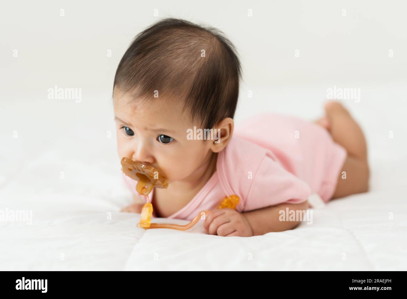 neonata sdraiata prona mentre succhia con il succhietto su un letto Foto Stock
