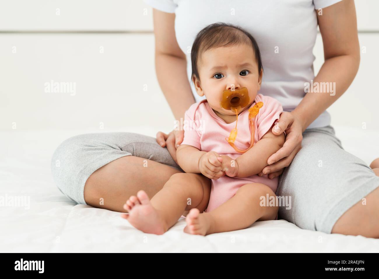 la neonata succhia un succhietto con la madre seduta su un letto Foto Stock