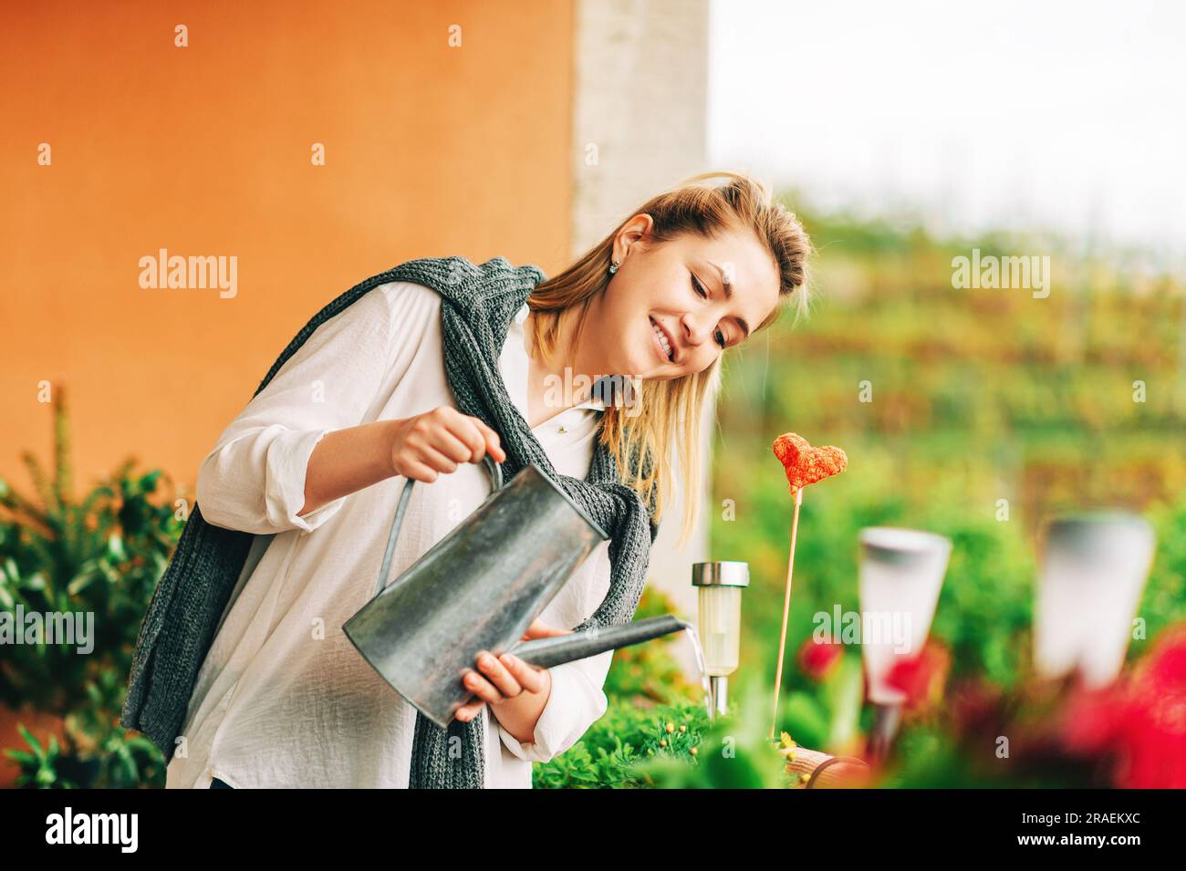 Ritratto di bella donna annaffiando piante verdi sul balcone, piccolo giardino accogliente in appartamento Foto Stock