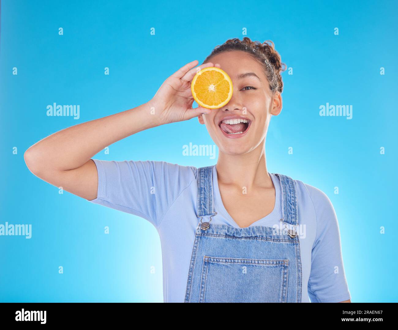 Ritratto, lingua fuori e donna con arancione in studio isolato su sfondo blu. Viso, frutta e persona con cibo per una dieta sana, nutrizione o. Foto Stock