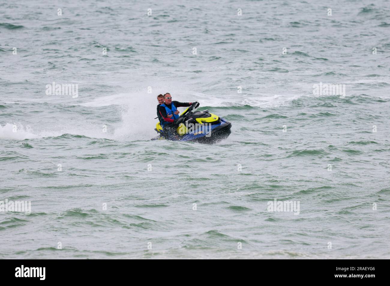 Moto d'acqua o moto d'acqua personale in mare con conducente e passeggero pillion appena al largo scafo nero blu e giallo occhi di carrozzeria chiusi sul passeggero Foto Stock