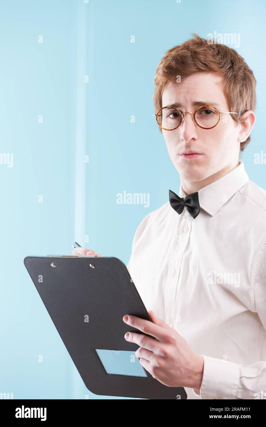 Un giovane con un vestito da ufficio vecchio stile, forse un nerd, un contabile leggermente servile, prende un blocco note. Il suo sguardo triste, la camicia bianca e il papillon sta Foto Stock