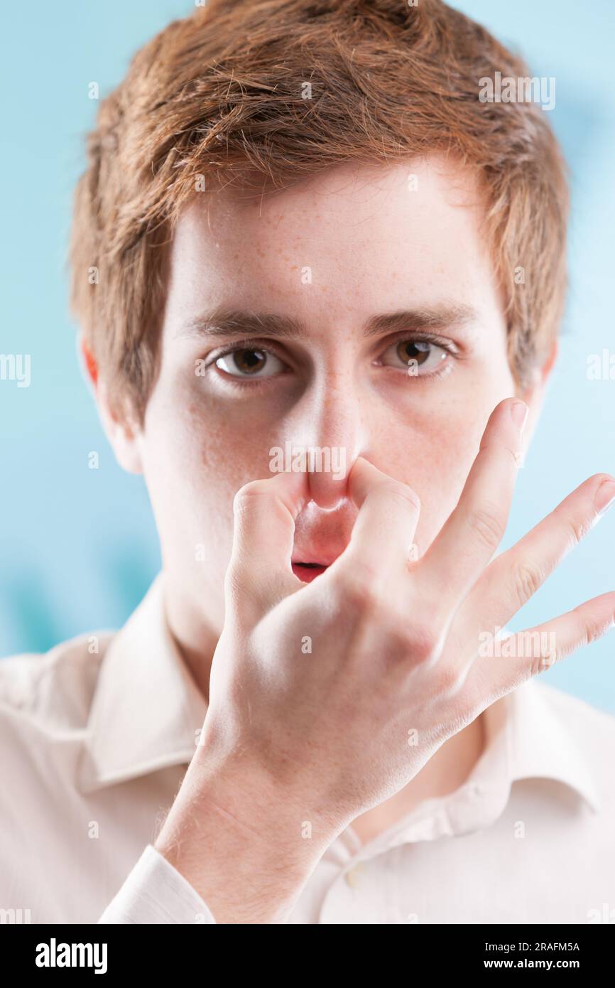 Un lavoratore d'ufficio dai capelli rossi con una camicia bianca gli stringe il naso in disgusto. In un contesto commerciale blu, ha pratiche non etiche per mantenere la sua jo Foto Stock