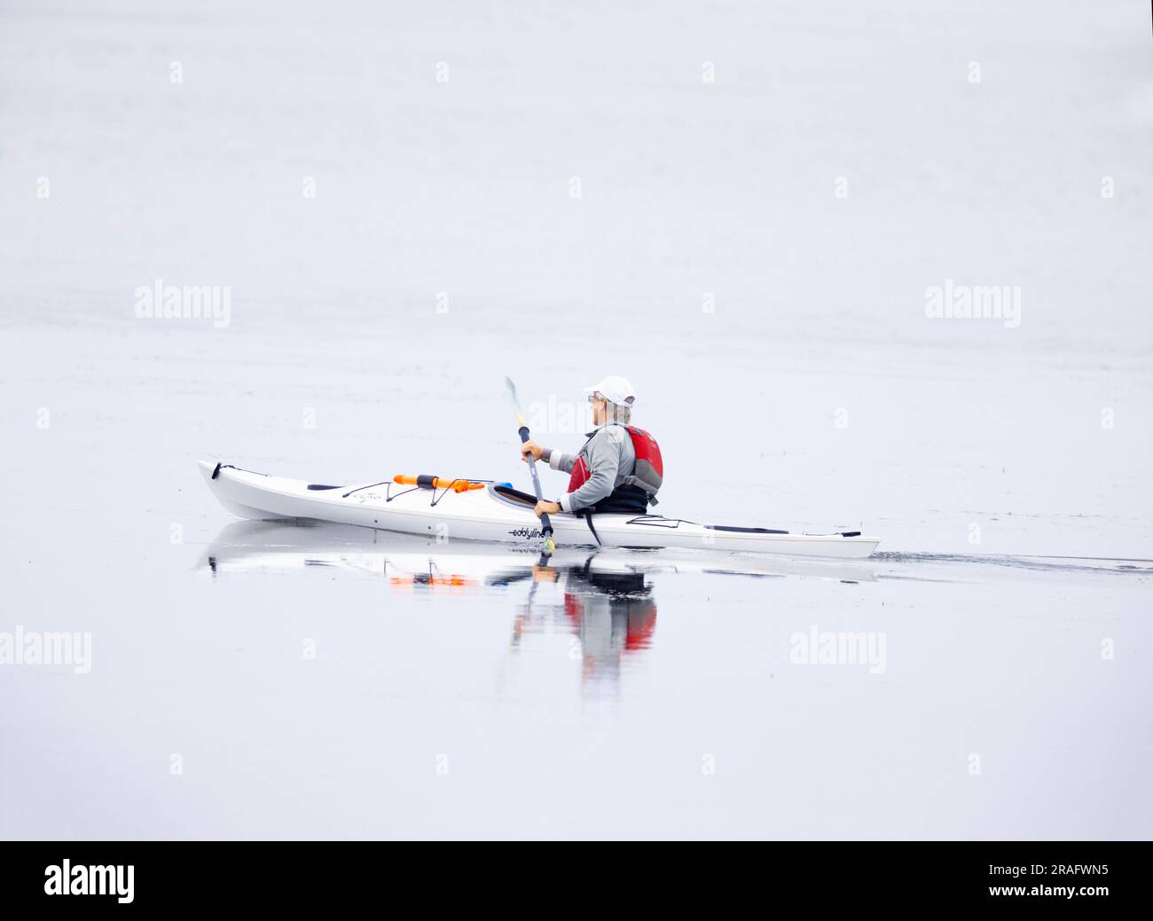 Uomo in kayak bianco che indossa un giubbotto salvagente rosso Foto Stock