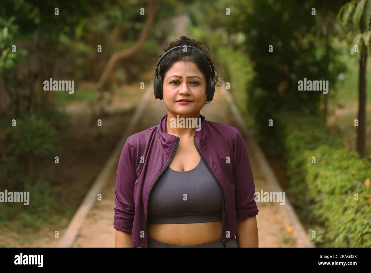 Donna anziana che fa jogging nel parco su una pista da jogging e un sentiero che si prende cura della sua salute. Sta ascoltando musica con le cuffie durante una pausa jogging Foto Stock
