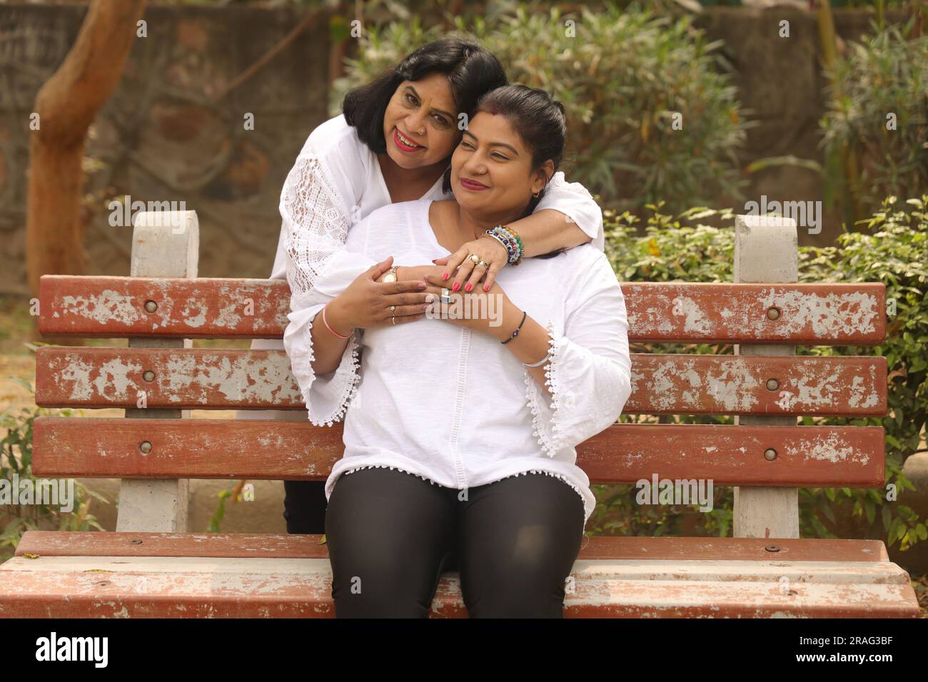 Madre e figlia indiana felici in abito bianco che trascorrono bellissimi momenti seduti sulla panchina nel parco cittadino. Madre amorevole e adorabile figlia. Foto Stock