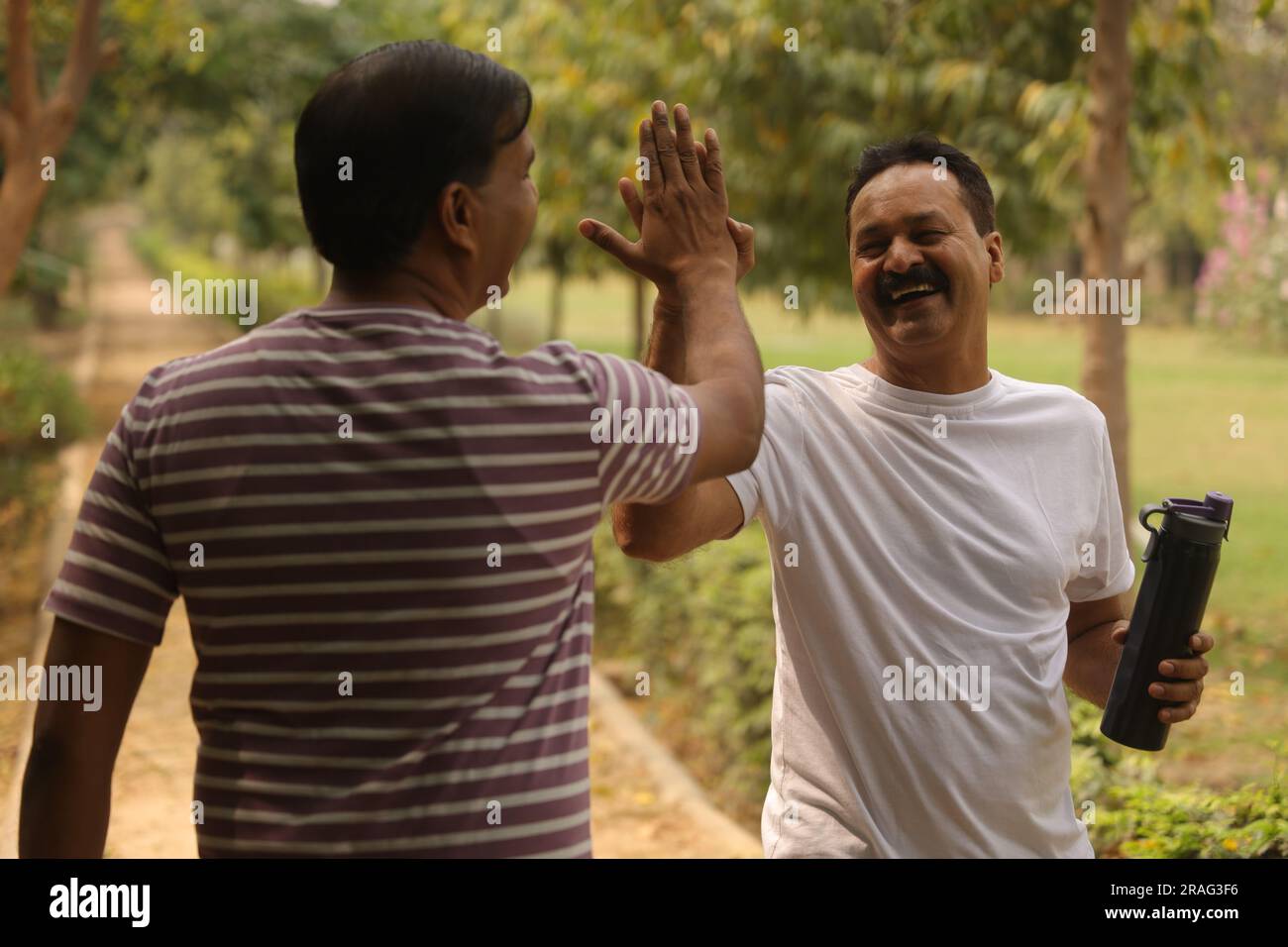 persone consapevoli della salute e amici che tifanno su mentre fanno jogging. Stanno facendo un saluto cinque di fronte l'uno all'altro, facendo jogging la mattina presto su una pista Foto Stock