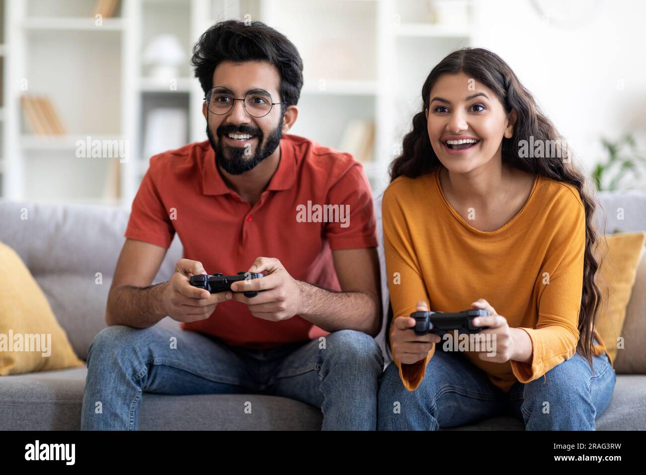 Giovane coppia indiana che gioca ai videogiochi con i joystick a casa Foto Stock