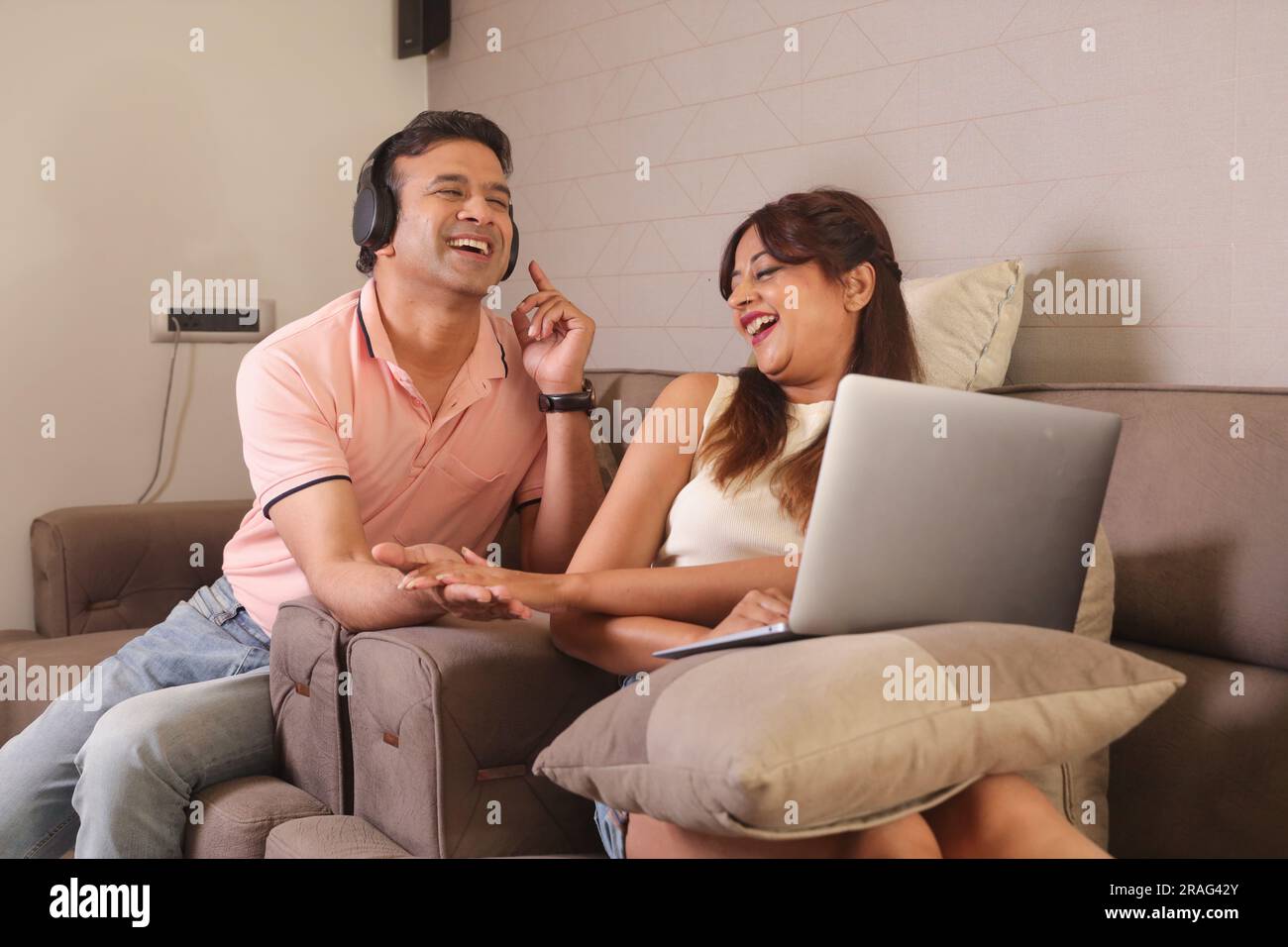 Indiano coppia felice mangiare insalata e dieta sana seduti su un divano tenendo un portatile navigare online. Ascolto di musica Foto Stock
