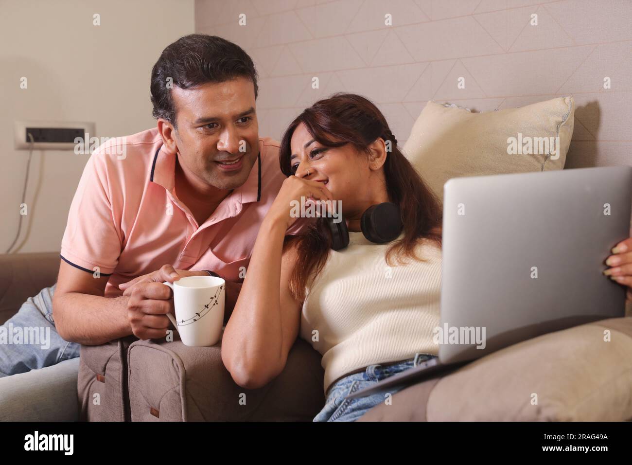 Coppia indiana felice seduta su un divano con un laptop che naviga online. E prendere una tazza di caffè e momenti felici. Foto Stock