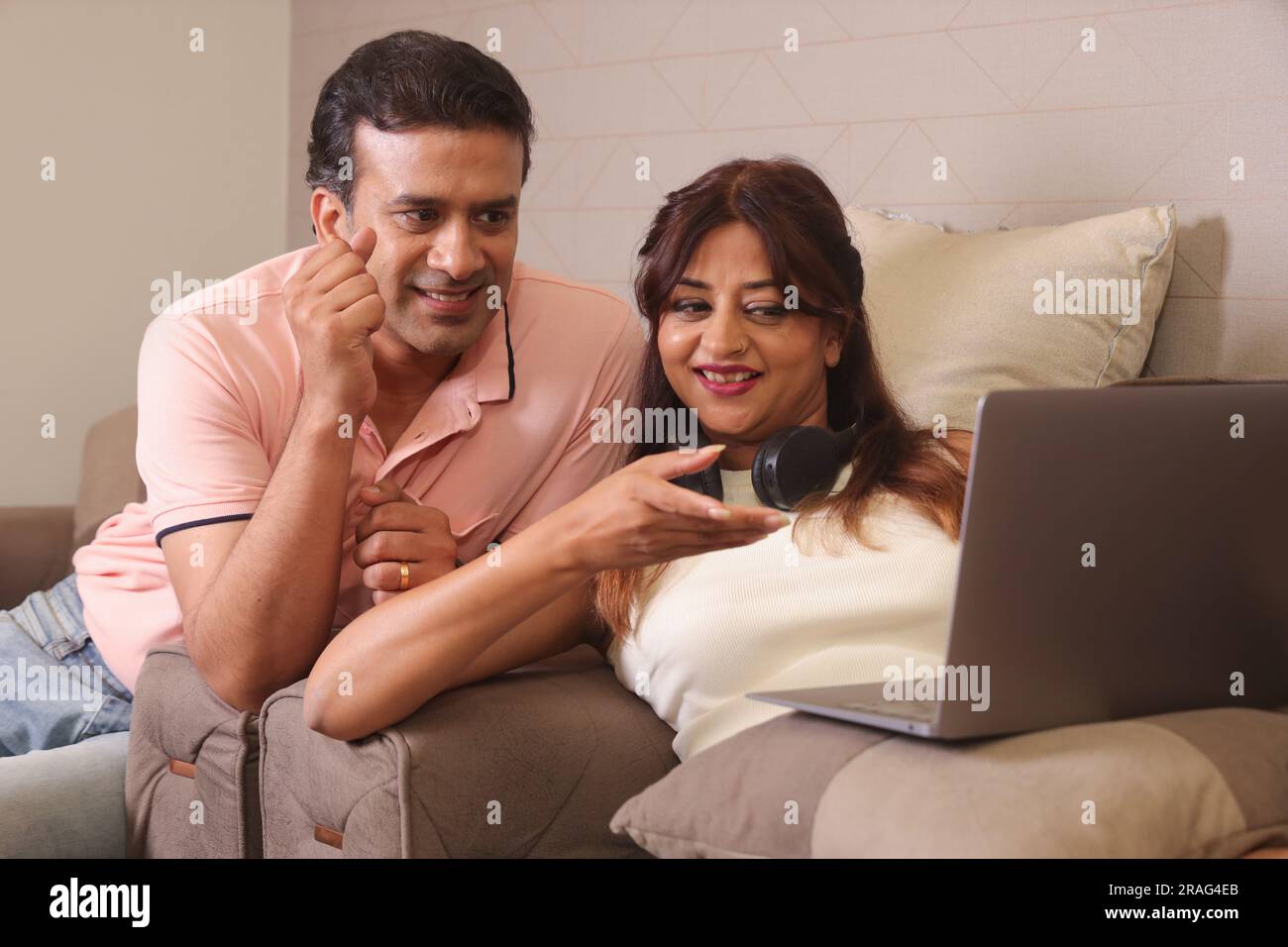Indiano coppia felice mangiare insalata e dieta sana seduti su un divano tenendo un portatile navigare online. Foto Stock