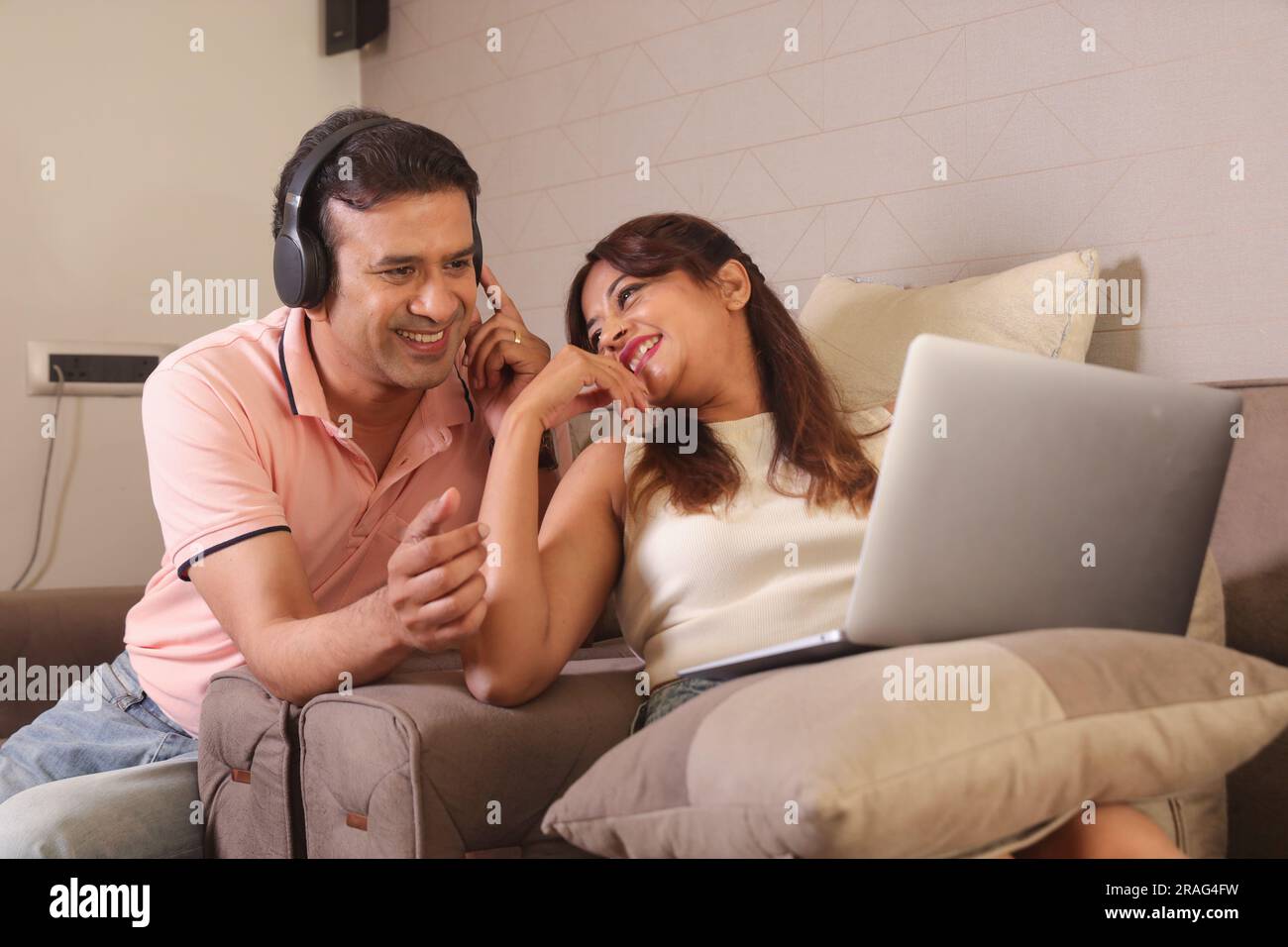 Indiano coppia felice mangiare insalata e dieta sana seduti su un divano tenendo un portatile navigare online. Ascolto di musica. Ascolto di canzoni. Foto Stock