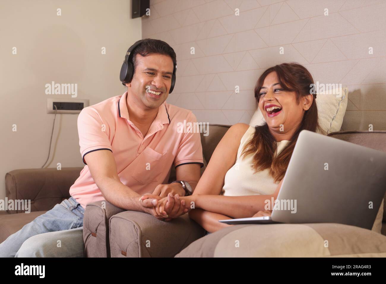 Indiano coppia felice mangiare insalata e dieta sana seduti su un divano tenendo un portatile navigare online. Ascolto di musica. Ascolto di canzoni. Foto Stock