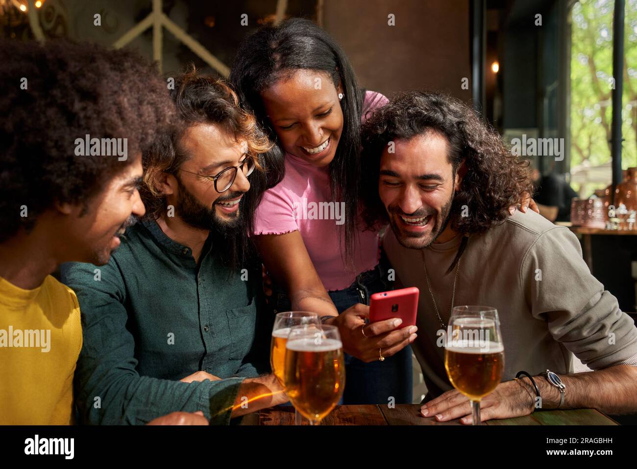 Giovane gruppo multietnico di persone che guardano un cellulare e sorridono in un bar. Foto Stock
