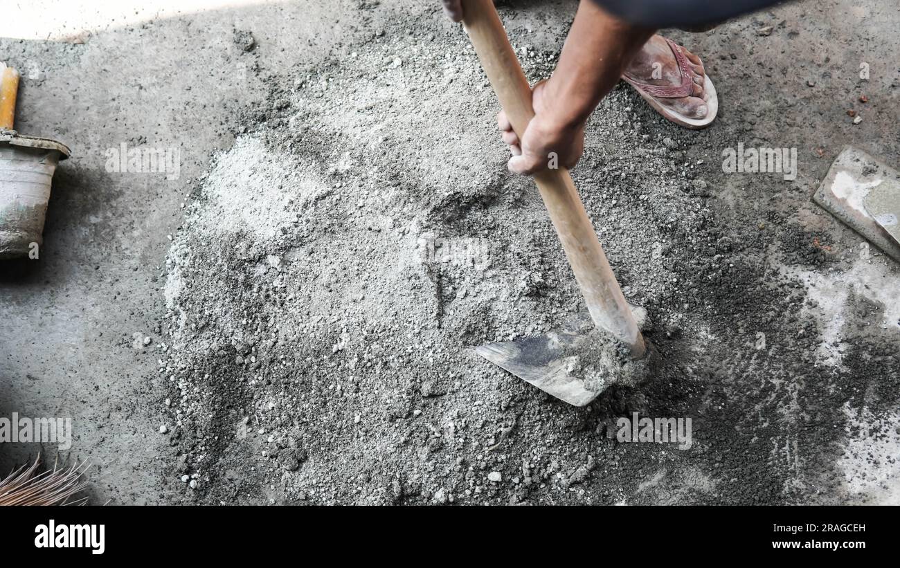 Lavoratore asiatico che utilizza zappa per miscelare la potenza del cemento con la sabbia Foto Stock