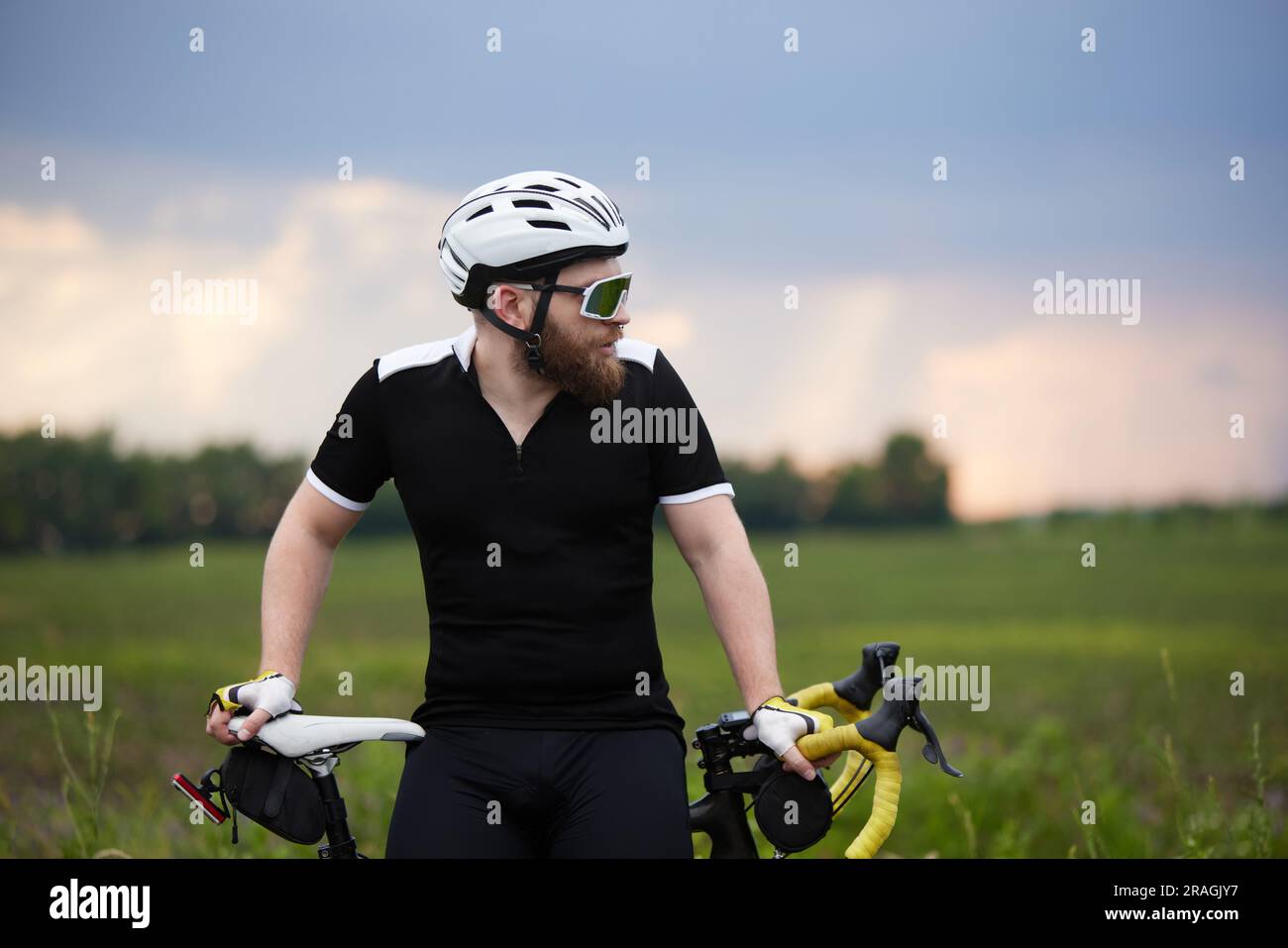 Elegante, sportivo, uomo barbuto in abbigliamento sportivo e casco, seduto  in bicicletta sulla strada in campo nelle serate estive più fredde Foto  stock - Alamy