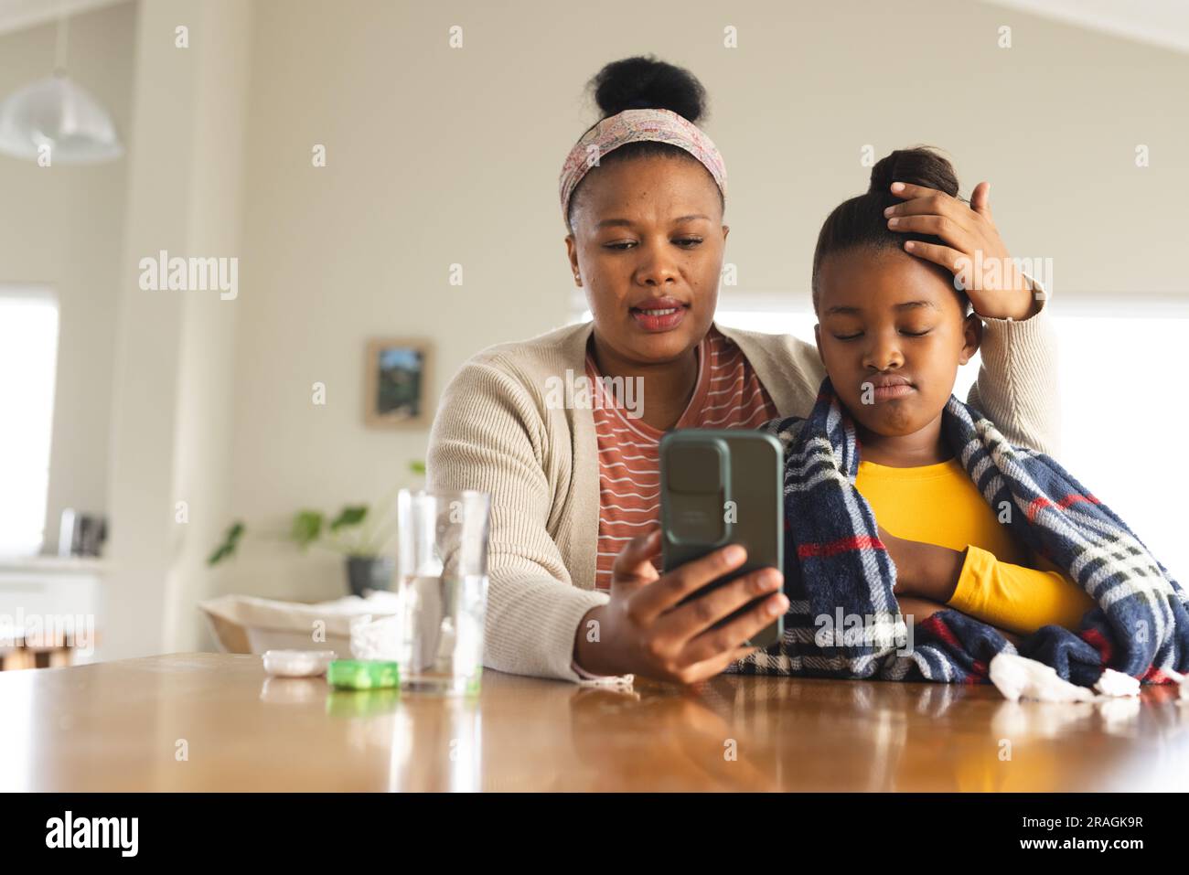 Madre e figlia afroamericana che utilizzano lo smartphone per la consultazione online con il medico Foto Stock
