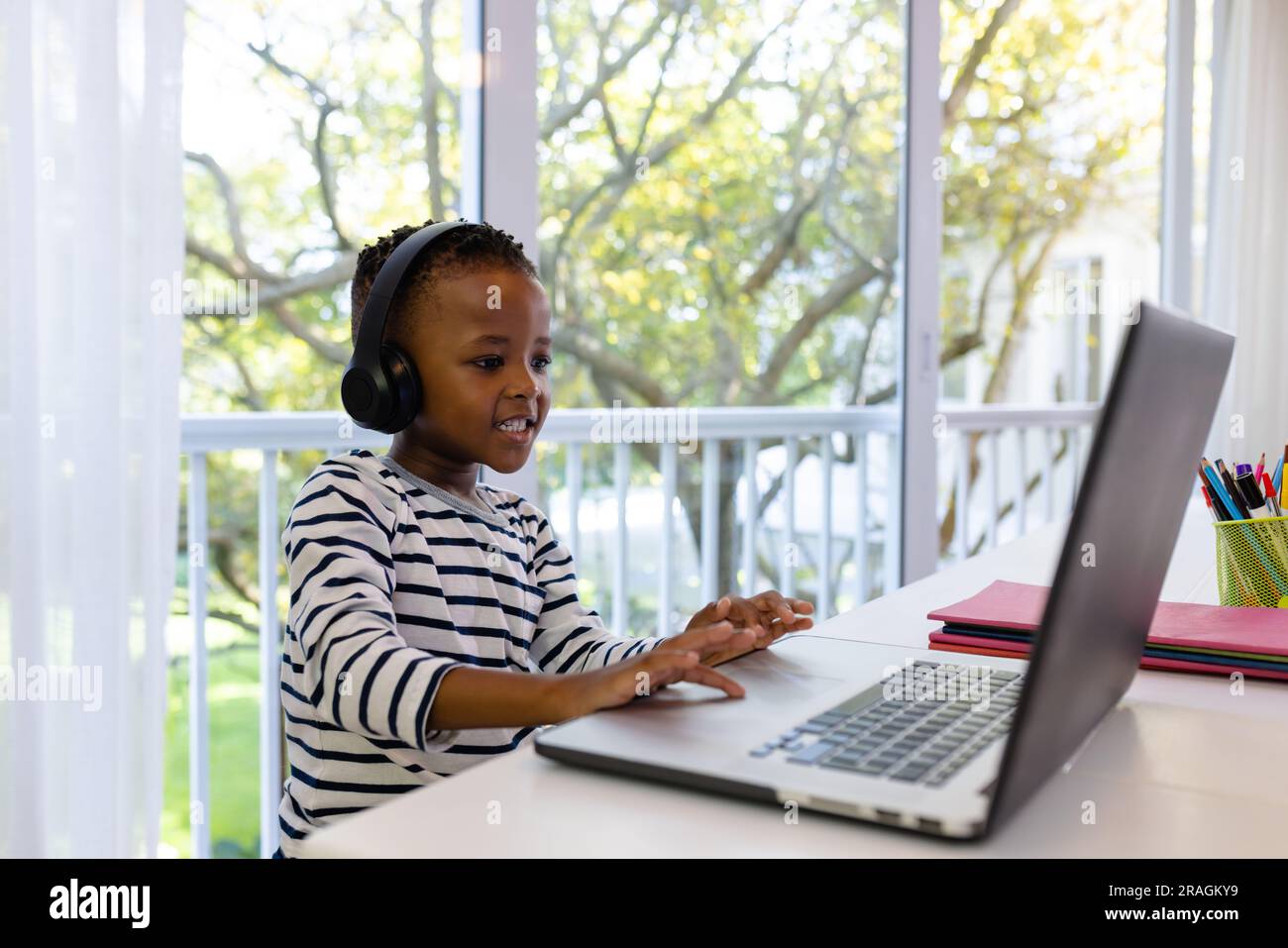 Ragazzo afro-americano sorridente che indossa gli auricolari e frequenta una lezione online su un laptop a casa Foto Stock