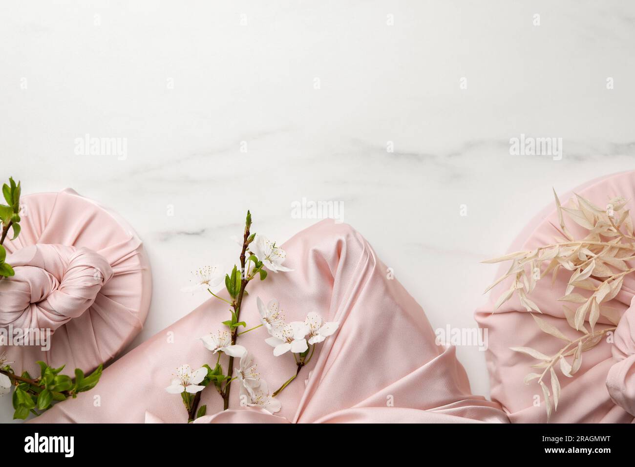 Tecnica Furoshiki. Regali confezionati in tessuto rosa su tavolo in marmo bianco, piatto. Spazio per il testo Foto Stock