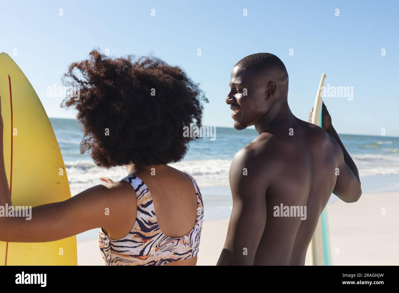 Felice coppia afro-americana con tavole da surf in piedi sulla spiaggia soleggiata a parlare Foto Stock