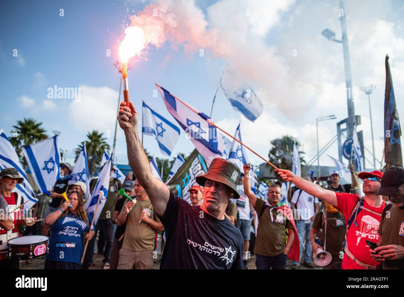 Haifa, Israele. 3 luglio 2023. Un protesta israeliano tiene una torcia mentre altri sventolano le bandiere israeliane durante una manifestazione contro la revisione giudiziaria che blocca il cancello del porto di Haifa. Promettendo di andare avanti con una giornata di proteste pianificate, nonostante Israele ridesse una grande operazione militare nella città di Jenin in Cisgiordania, i manifestanti contro lo sforzo del governo di rivedere il sistema giudiziario hanno bloccato l'accesso al porto di Haifa, dato che decine di raduni si sono svolti anche all'estero. Credito: SOPA Images Limited/Alamy Live News Foto Stock