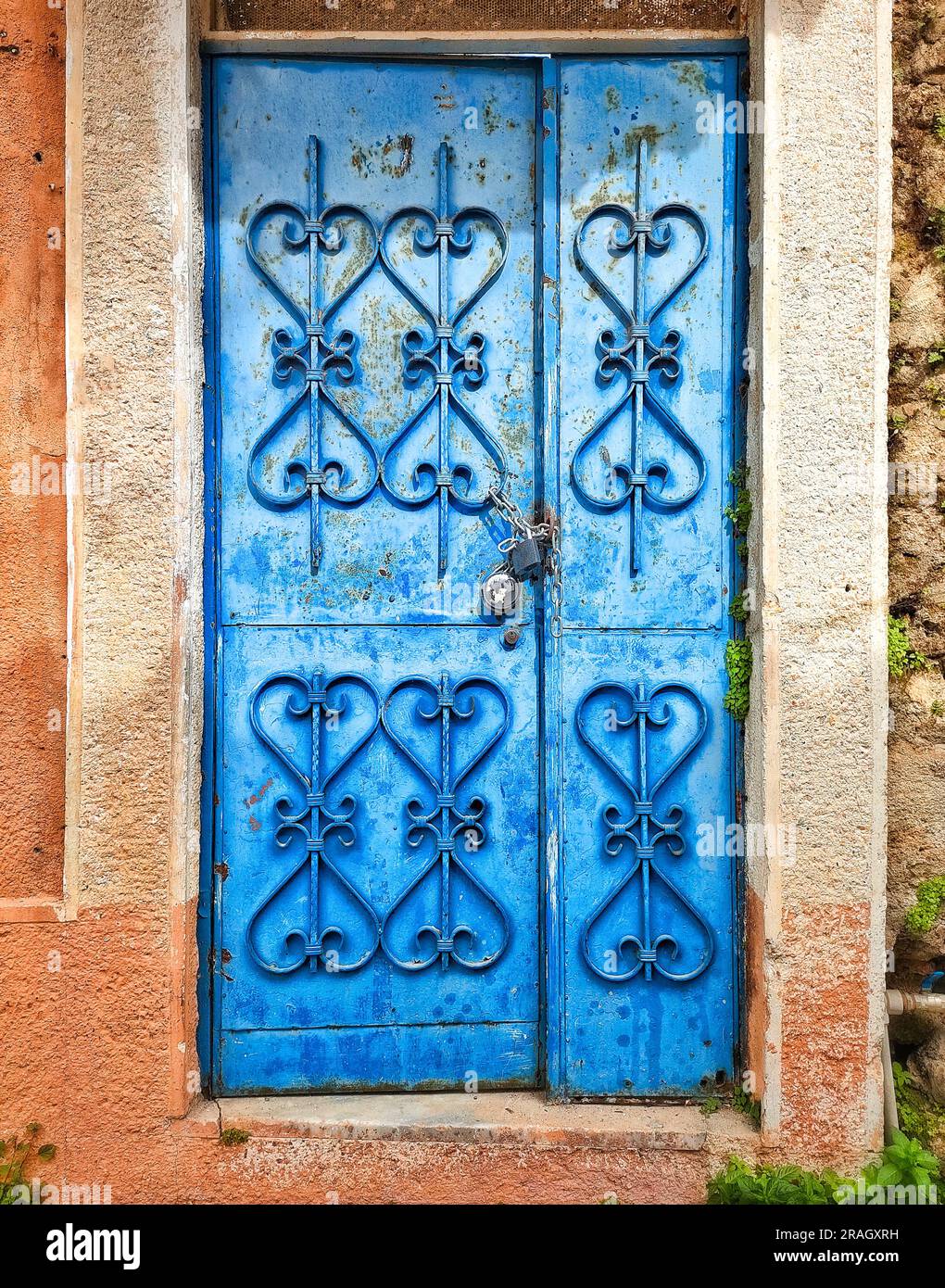 Porta anticata blu con forgiatura a motivi geometrici, chiusa con lucchetto, sullo sfondo della parete in pietra Foto Stock