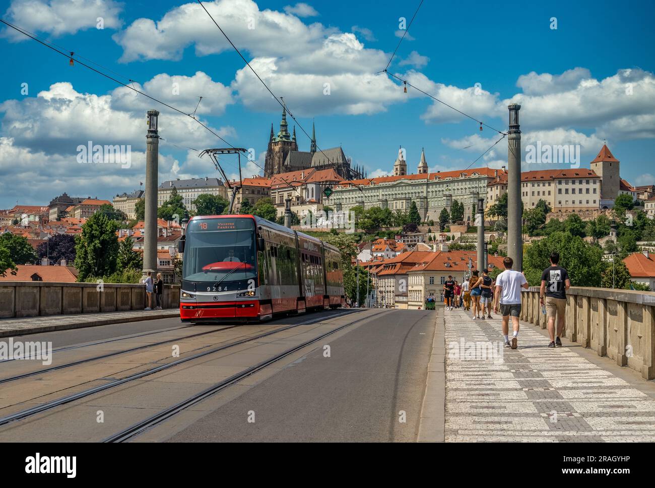 Il tram rosso attraversa il ponte di Manes con il castello di Praga sullo sfondo Foto Stock