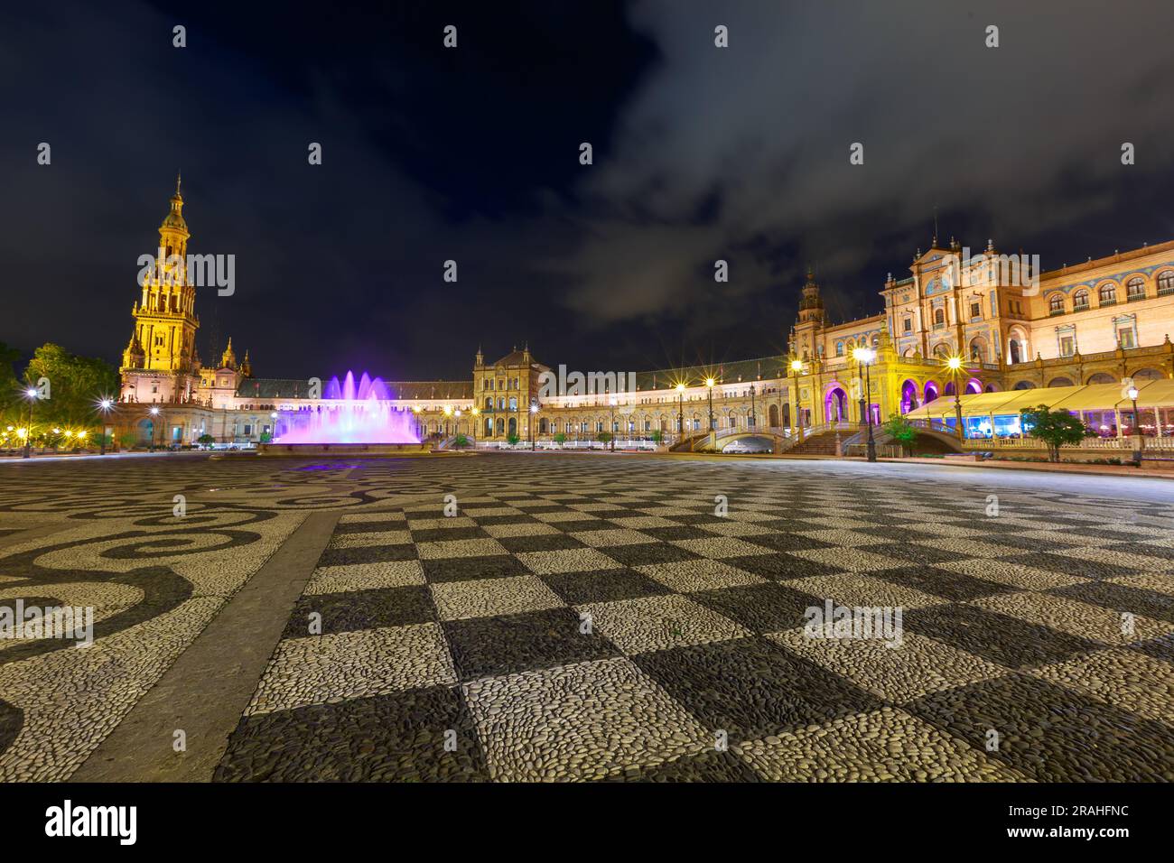 Fontana illuminata di notte in Plaza de Espana della città di Siviglia in Spagna, con acqua in movimento viola. Foto Stock